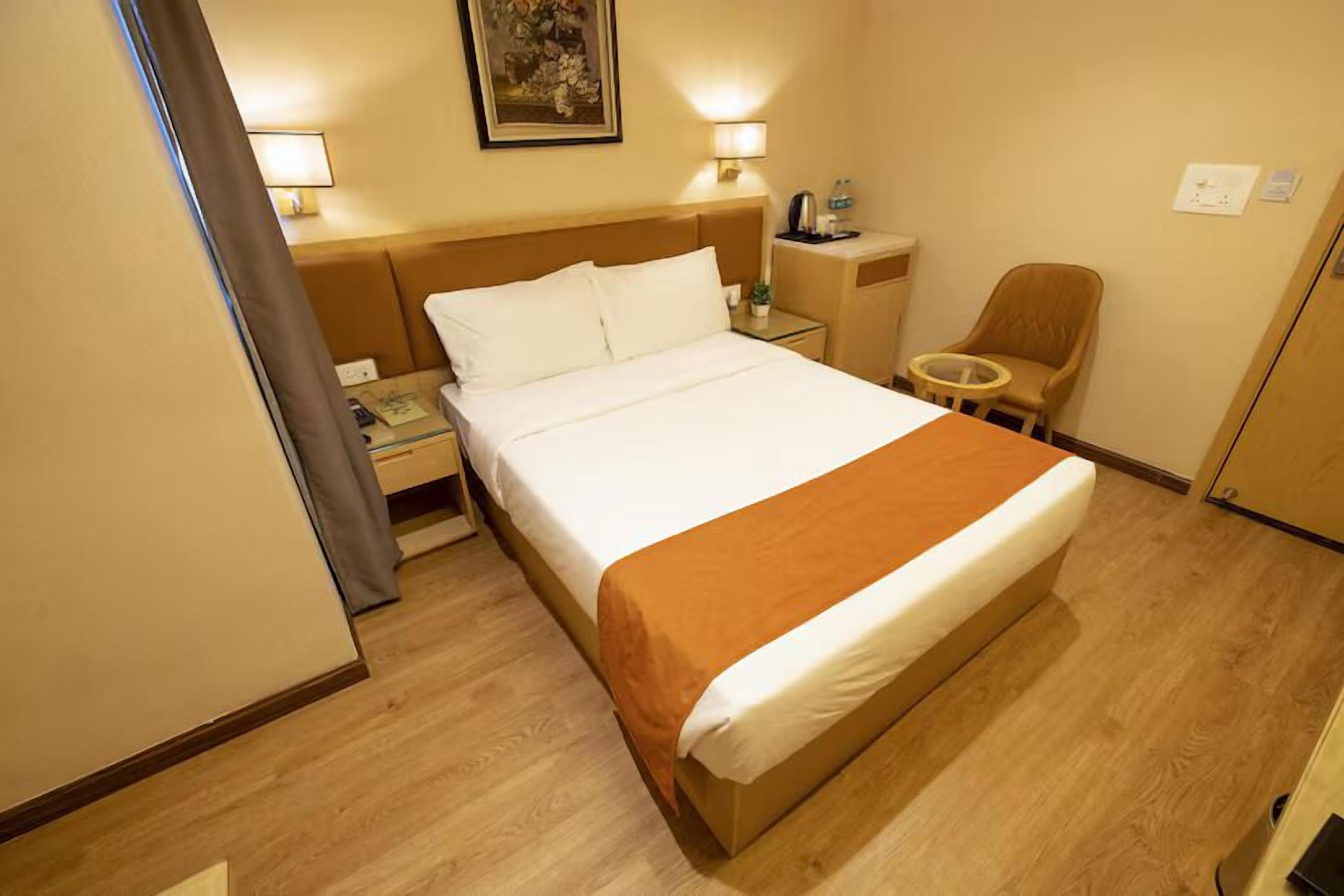 Quarto de hotel com cama, mesa de cabeceira, cadeira e um quadro na parede.