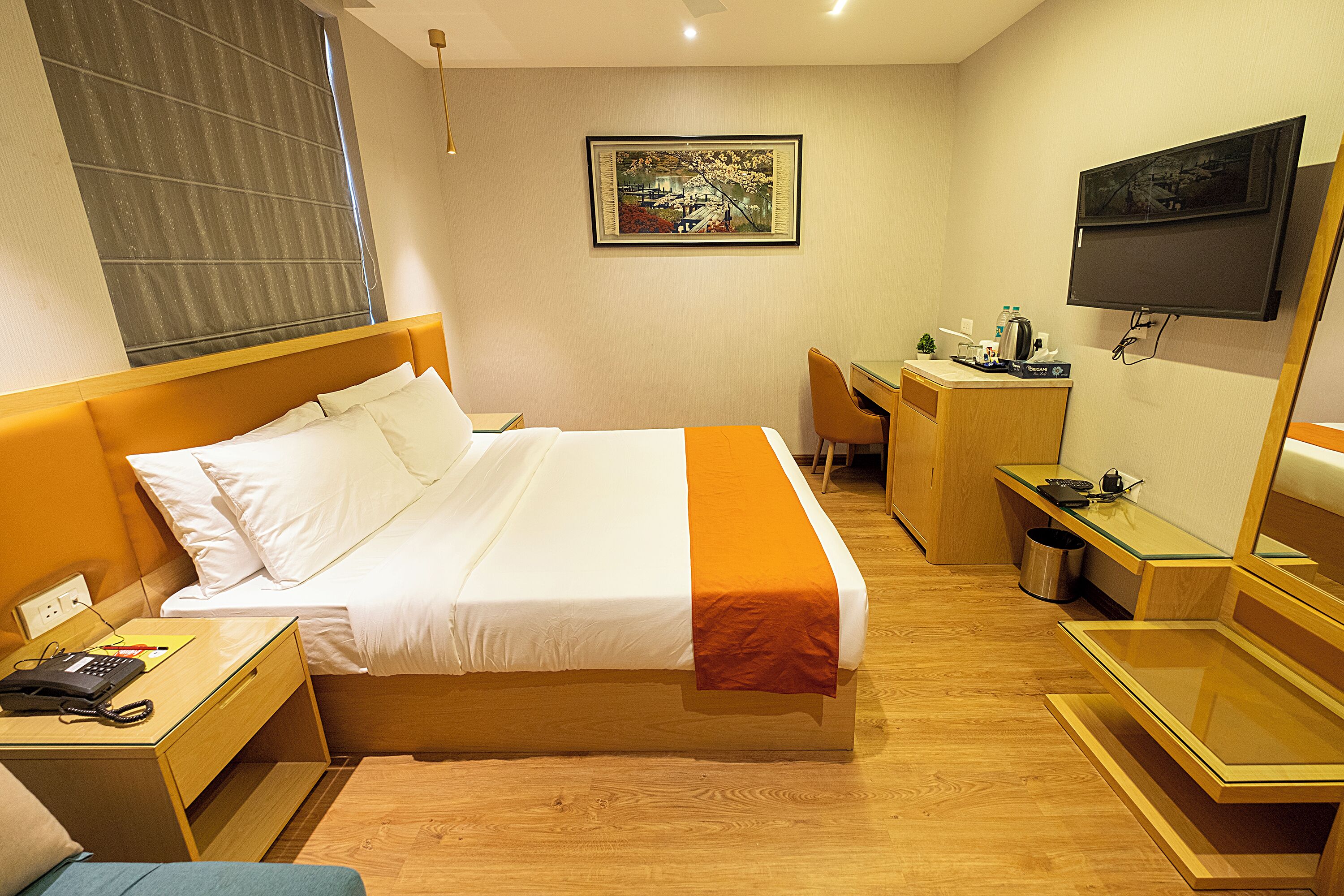 Habitación de hotel con cama, mesita de noche, escritorio, silla y televisor montado en la pared.