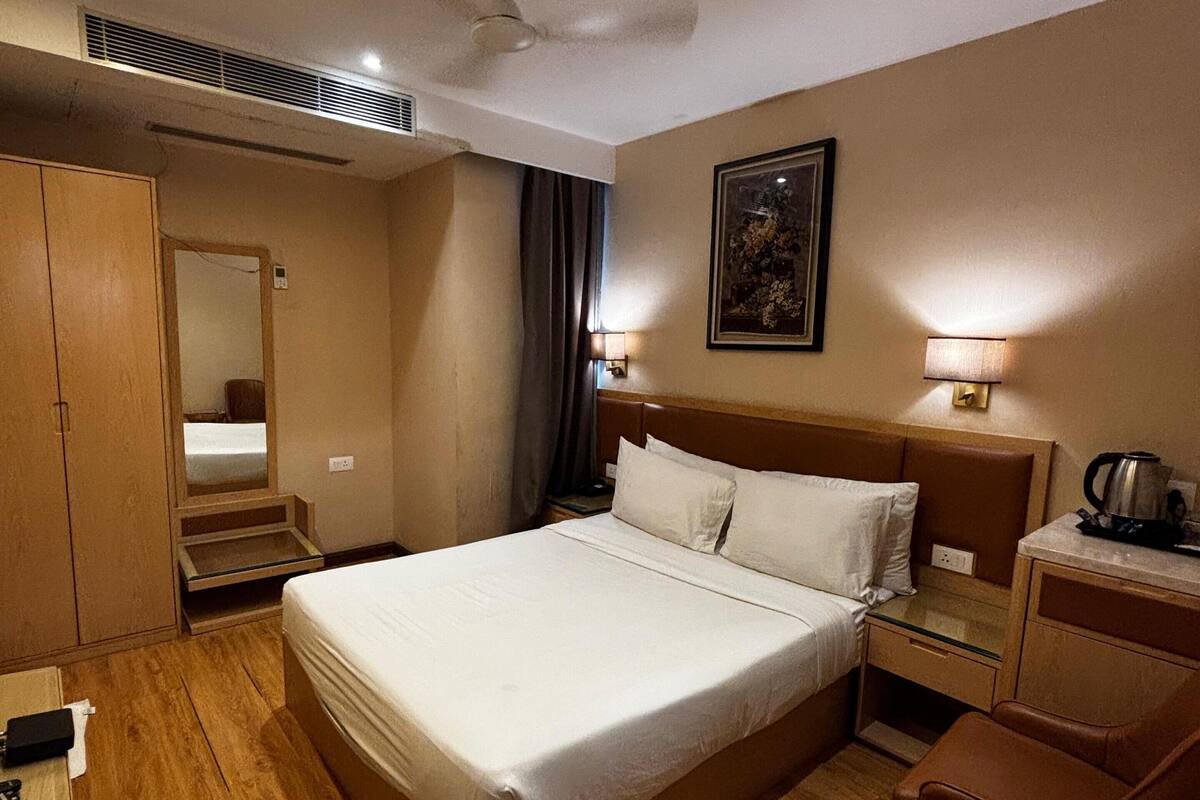 Habitación de hotel con una cama grande, mesitas de noche, un escritorio, una silla, un armario y un ventilador de techo.
