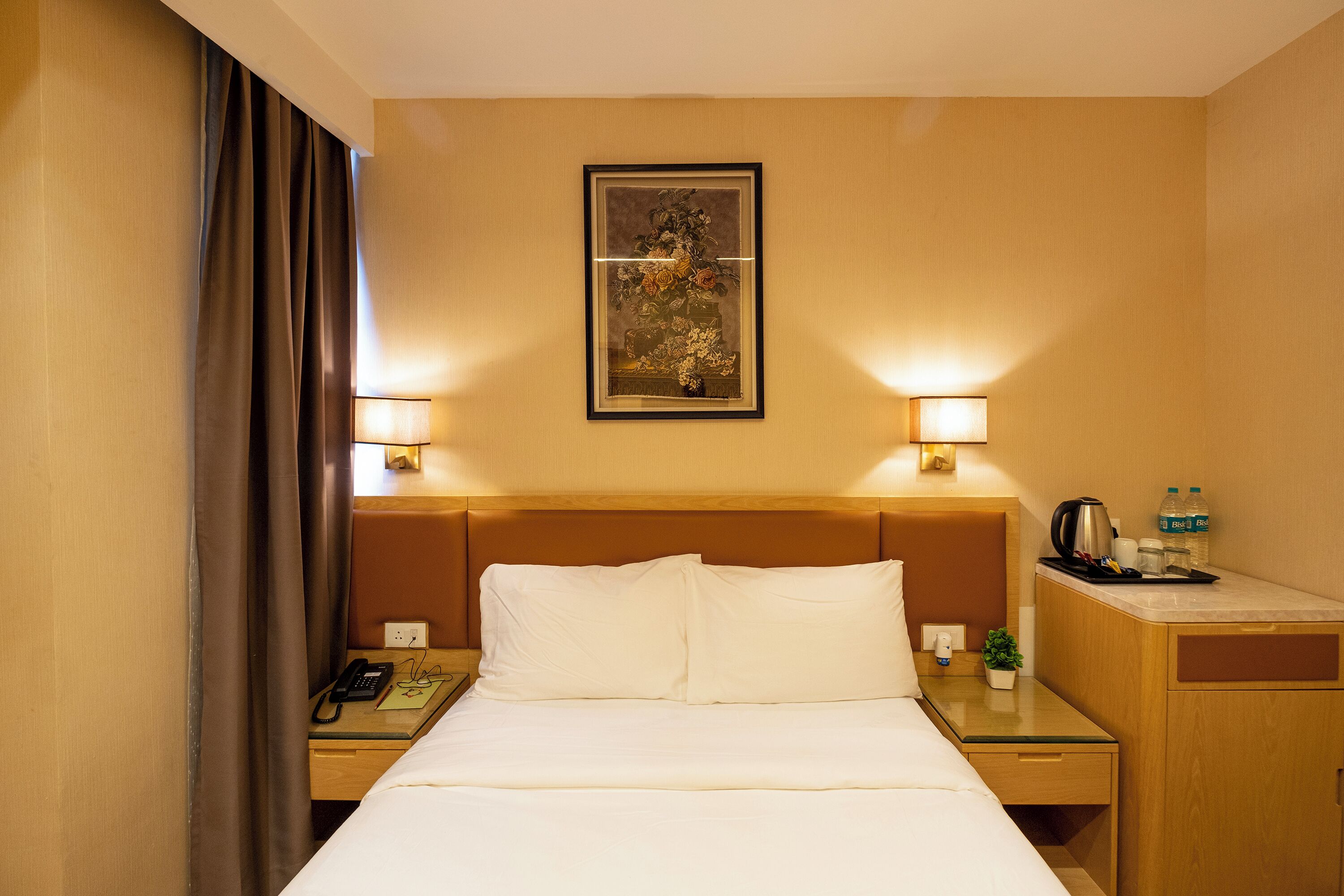 A hotel room with a bed, bedside lamps, a nightstand, a coffee maker, and a framed artwork on the wall.