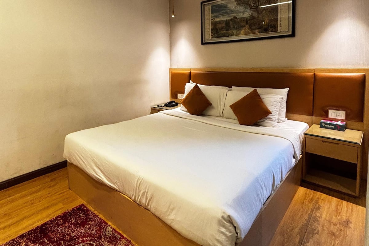 Una cama bien hecha con sábanas blancas, cabecera marrón y un cuadro en la pared.