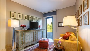 Een woonkamer met een televisie, een rode poef, een tapijt met patroon en een bank met een rode kussen.