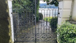 A wrought iron gate leading to a paved area with a stone wall and a statue on the right. - Vacation apartment Brissago (Brissago)