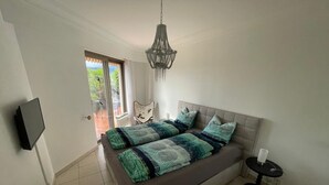 A bedroom with a bed, a TV mounted on the wall, a chandelier, and a view of the outdoors through a sliding door. - Vacation apartment Brissago (Brissago)