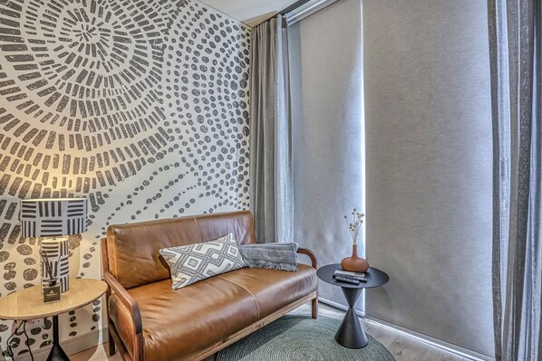 Una sala de estar moderna con un sofá de cuero, papel tapiz estampado, una mesita redonda y un ventanal con cortinas.