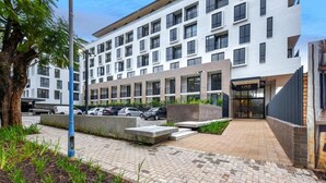 Un hotel moderno con fachada blanca, varios balcones y un estacionamiento.