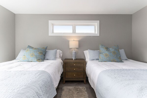A bedroom with two beds, a nightstand, a lamp, and a window. - The Birches Condotel Unit 2 (Lake Leelanau)