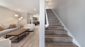 Una sala de estar moderna con un sofá, un sillón redondo y un banco. Hay una escalera con escalones de madera que sube a un piso superior.