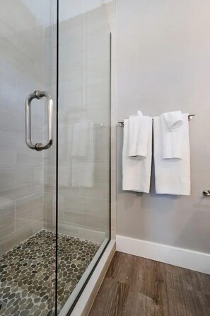 A glass-enclosed shower with a metal handle, a tiled floor, and two white towels hanging on a rack. - The Birches Condotel Unit 2 (Lake Leelanau)