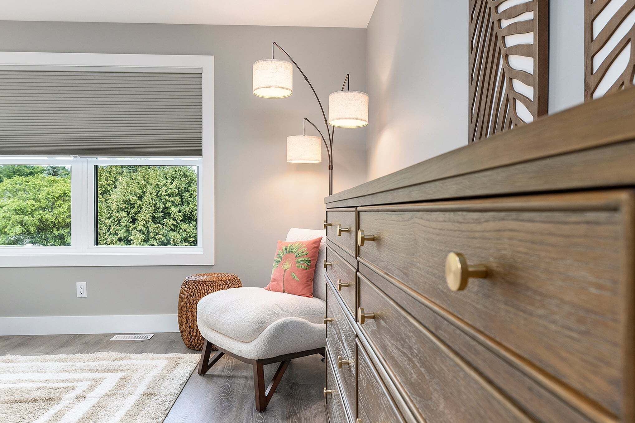 A room with a large window, a wooden dresser, a chair, and a decorative wall panel.