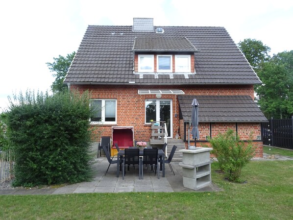 A brick house with a tiled roof, a patio with a table and chairs, and a small garden area.