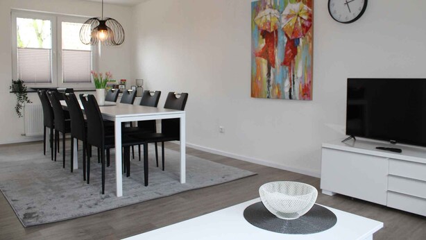 A modern living room with a dining area, a TV, and artwork on the wall.