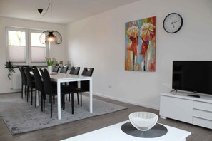 A modern living room with a dining area, a TV, and artwork on the wall.