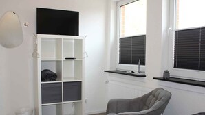 A room with a white wardrobe, a grey armchair, and a bed with a grey headboard.