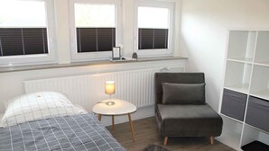 A bedroom with a bed, bedside table, lamp, chair, and built-in shelving.