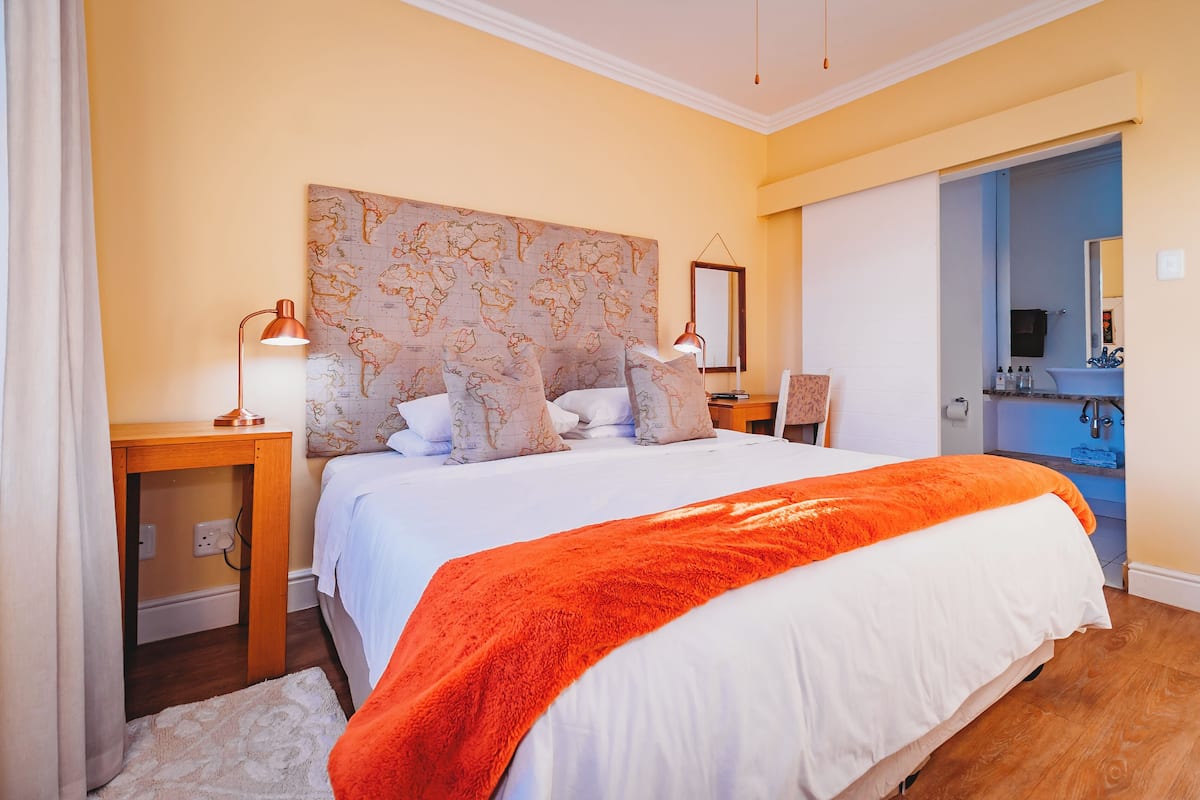 A hotel room with a large bed, a map headboard, a bathroom with a sink and mirror, and a nightstand with a lamp.