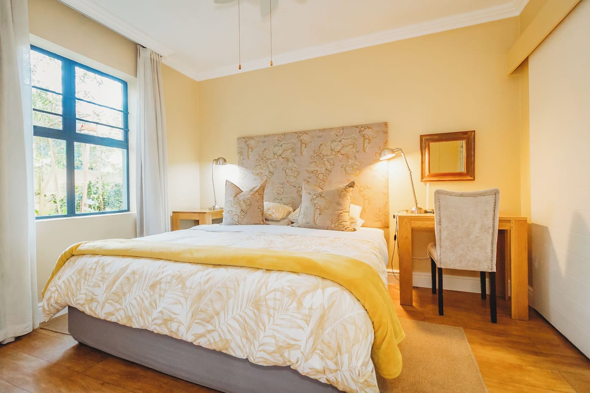 A bedroom with a bed, bedside lamps, a chair, a desk, and a window with curtains.