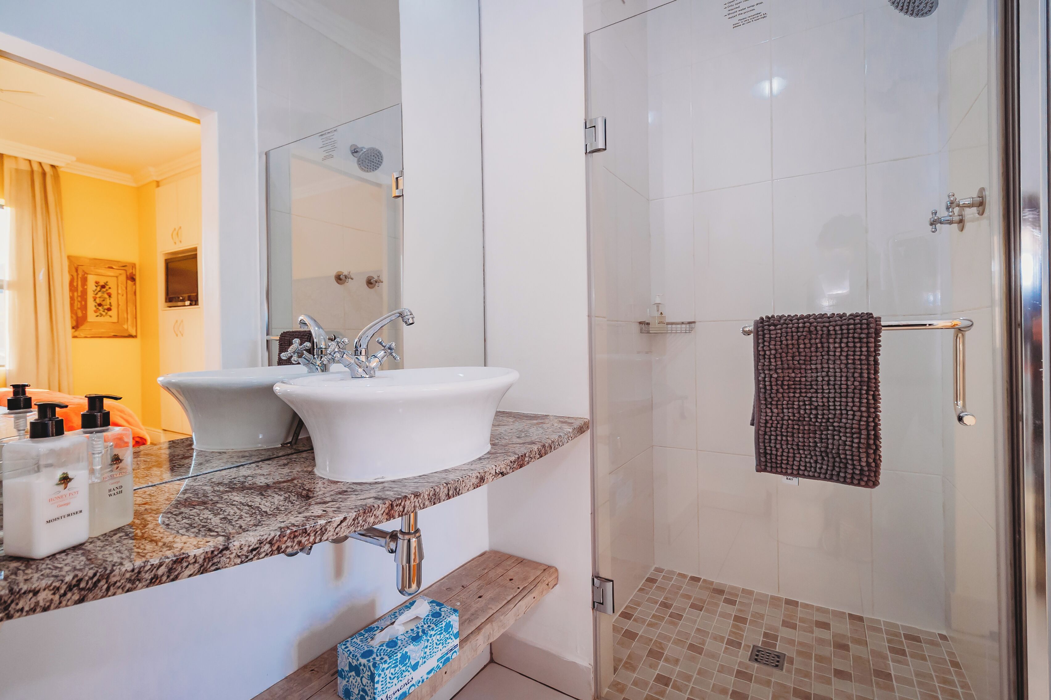 A bathroom with a white sink, a mirror, a shower with a glass door, and a towel rack.