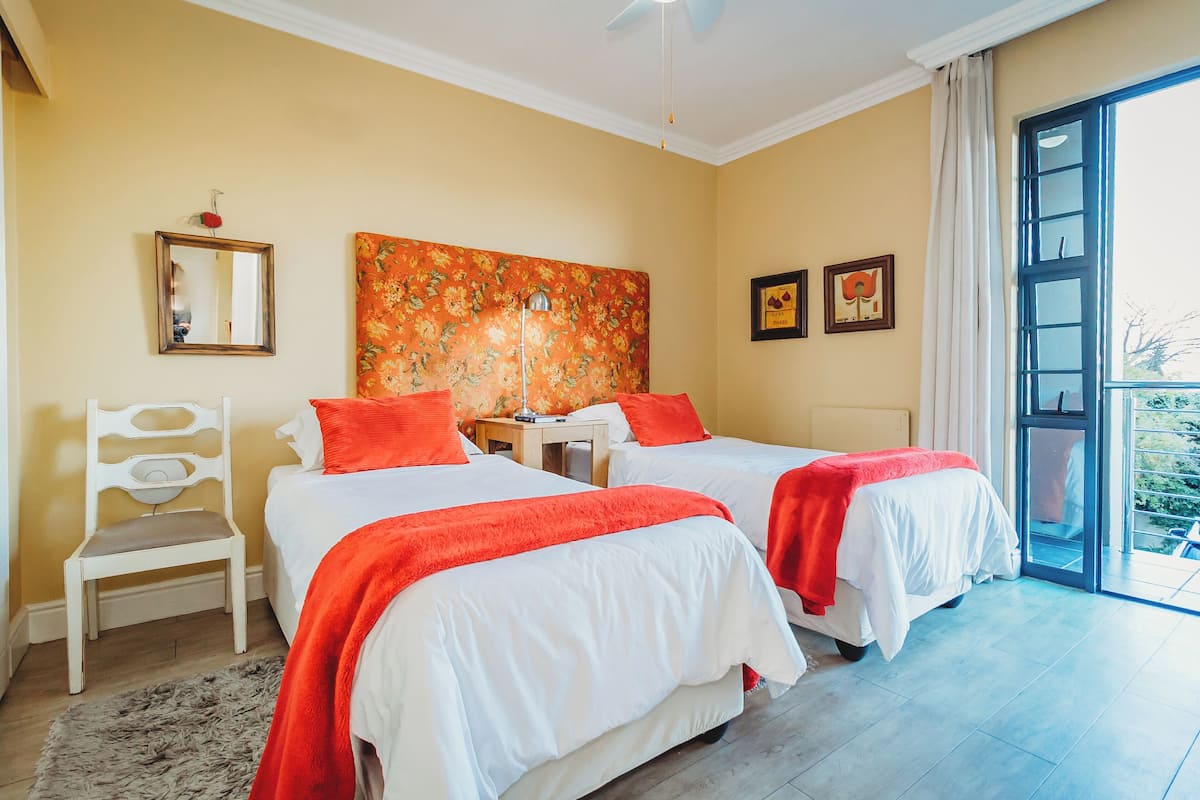 A hotel room with two beds, a chair, a large window, and artwork on the wall.