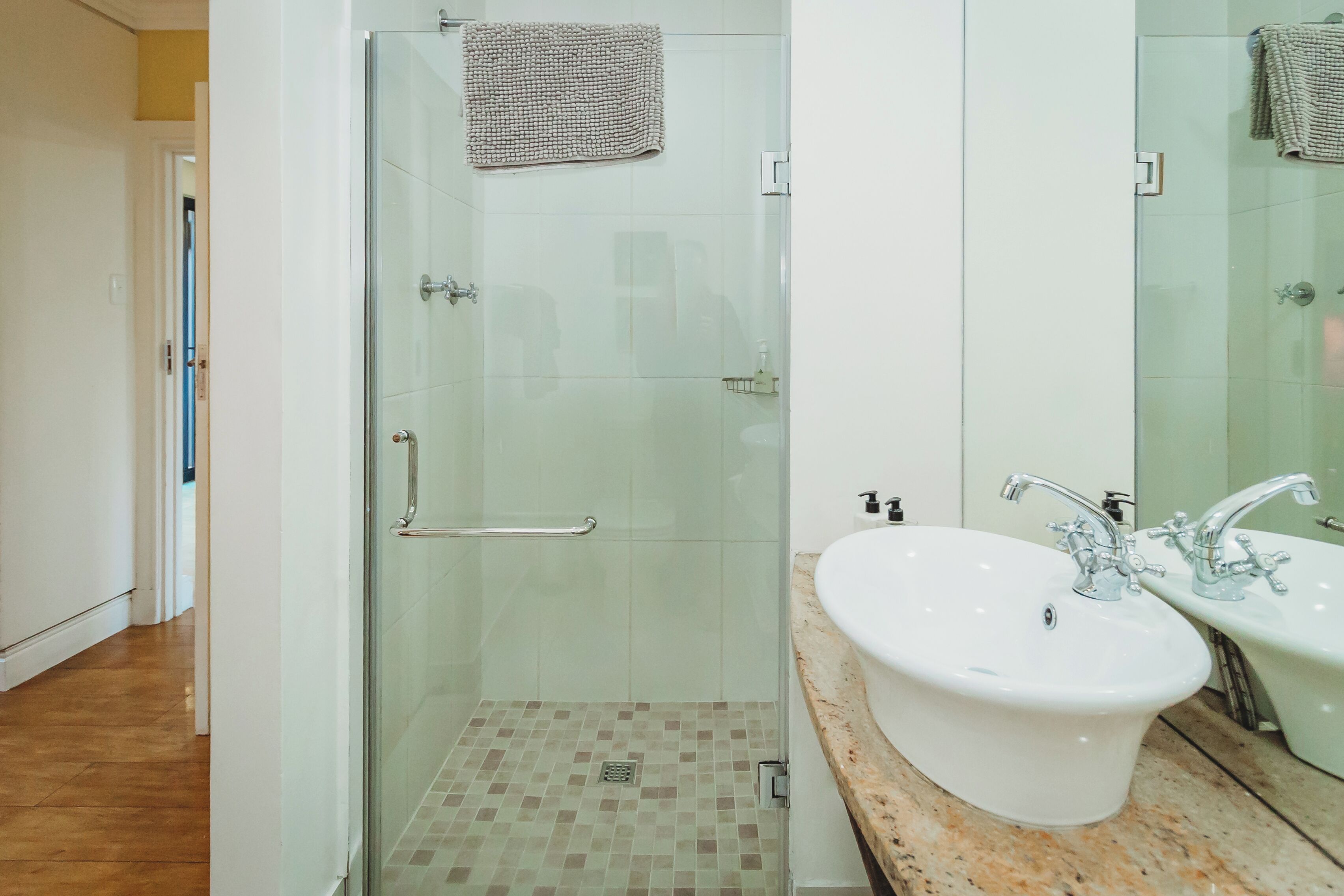 Un baño moderno con ducha de vidrio, lavamanos blanco con dos grifos y un espejo grande.