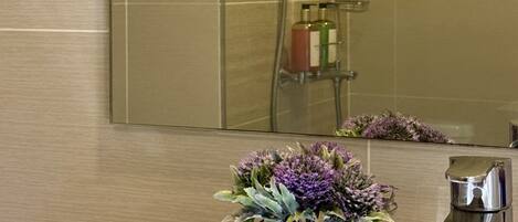 A bathroom with a shower, a sink with a faucet, and a vase with flowers on the counter.