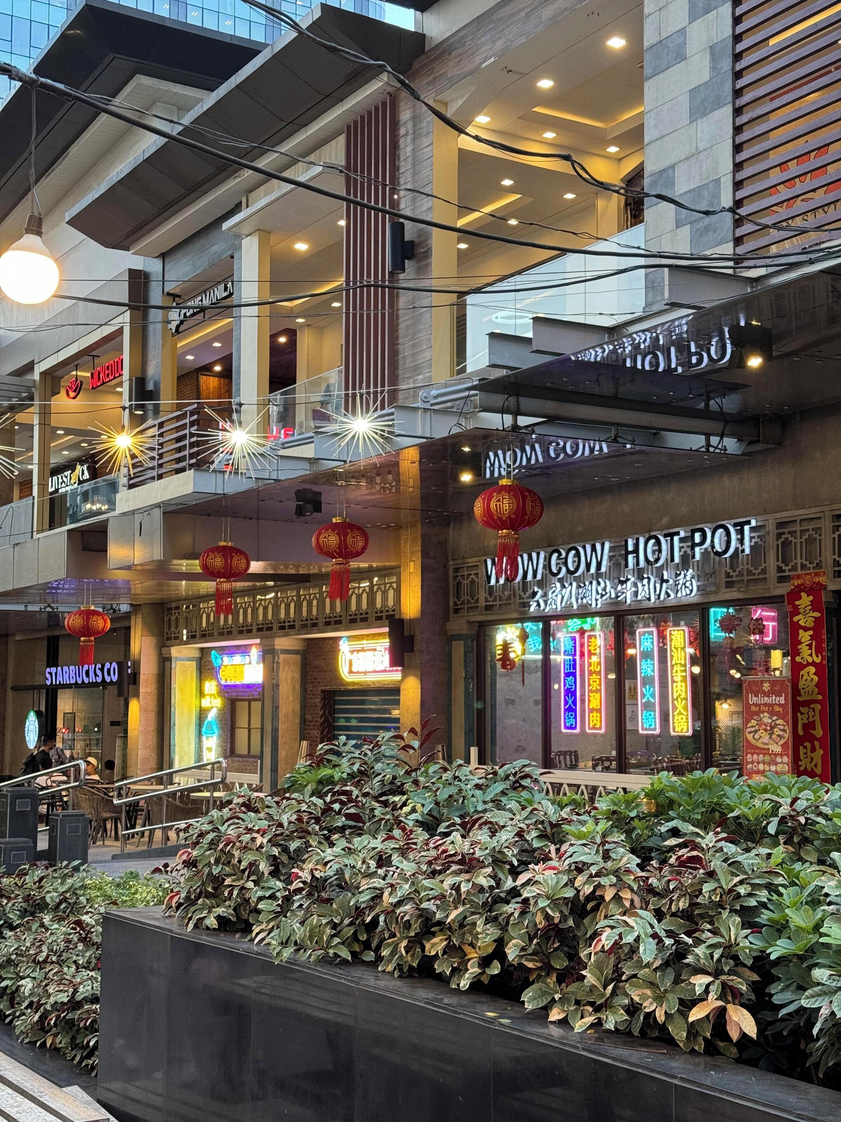 Un edificio comercial de varios niveles con diversas tiendas, incluyendo Starbucks y un restaurante llamado “WOW COW HOT POT”.