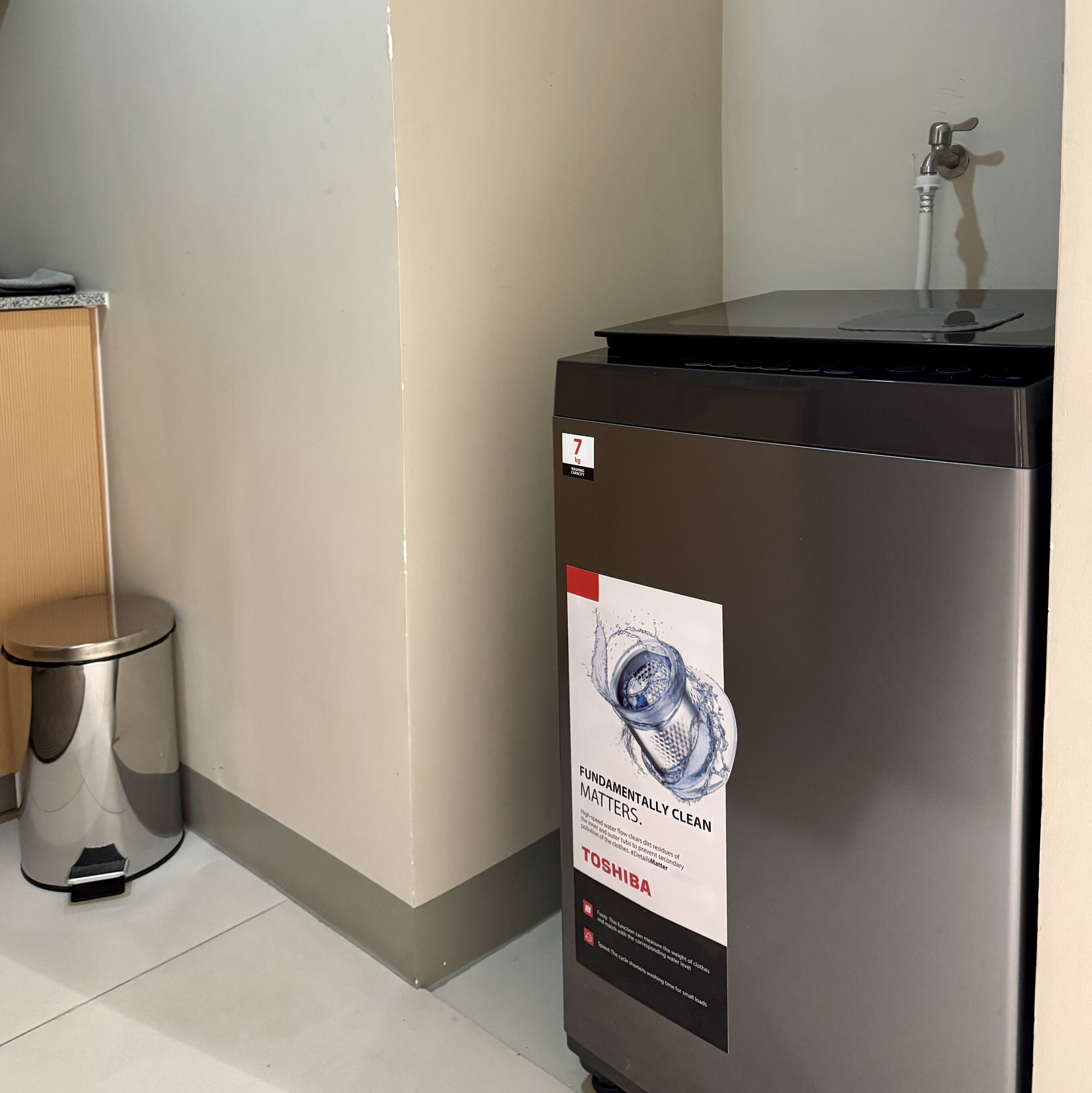 A compact, stainless steel trash bin with a water filtration label, placed next to a wall and a small trash can.