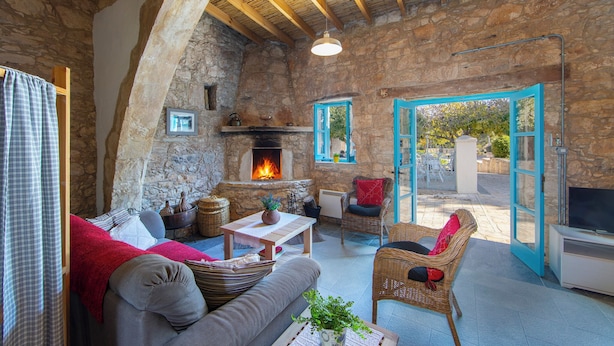 A rustic stone interior with a fireplace, wicker furniture, and a television. - AKAMANTIDA PLATEA 1. A 3-bedroom country house built in 1900, renovated in 2016. (Pano Arodes)