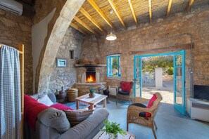 A rustic stone interior with a fireplace, wicker furniture, and a television. - AKAMANTIDA PLATEA 1. A 3-bedroom country house built in 1900, renovated in 2016. (Pano Arodes)