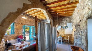 A rustic interior with stone walls, wooden beams, a dining area, and a cozy seating space. - AKAMANTIDA PLATEA 1. A 3-bedroom country house built in 1900, renovated in 2016. (Pano Arodes)