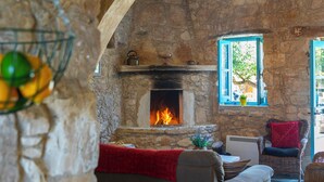 A stone-walled room with a fireplace, wicker furniture, and a red throw blanket. - AKAMANTIDA PLATEA 1. A 3-bedroom country house built in 1900, renovated in 2016. (Pano Arodes)