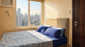 Une chambre à coucher avec un lit, une fenêtre donnant sur la ville, une porte et un appareil de climatisation fixé au mur.