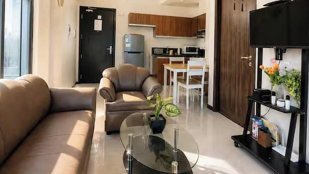 Un salon moderne avec un canapé, une table basse en verre et un coin repas comprenant une table et des chaises blanches.