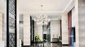 Een ruime lobby met een spiegelende vloer, een centraal hanglamp en een decoratief wandpaneel.