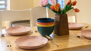 A dining table with pink plates, a colorful bowl, and a vase with tulips.