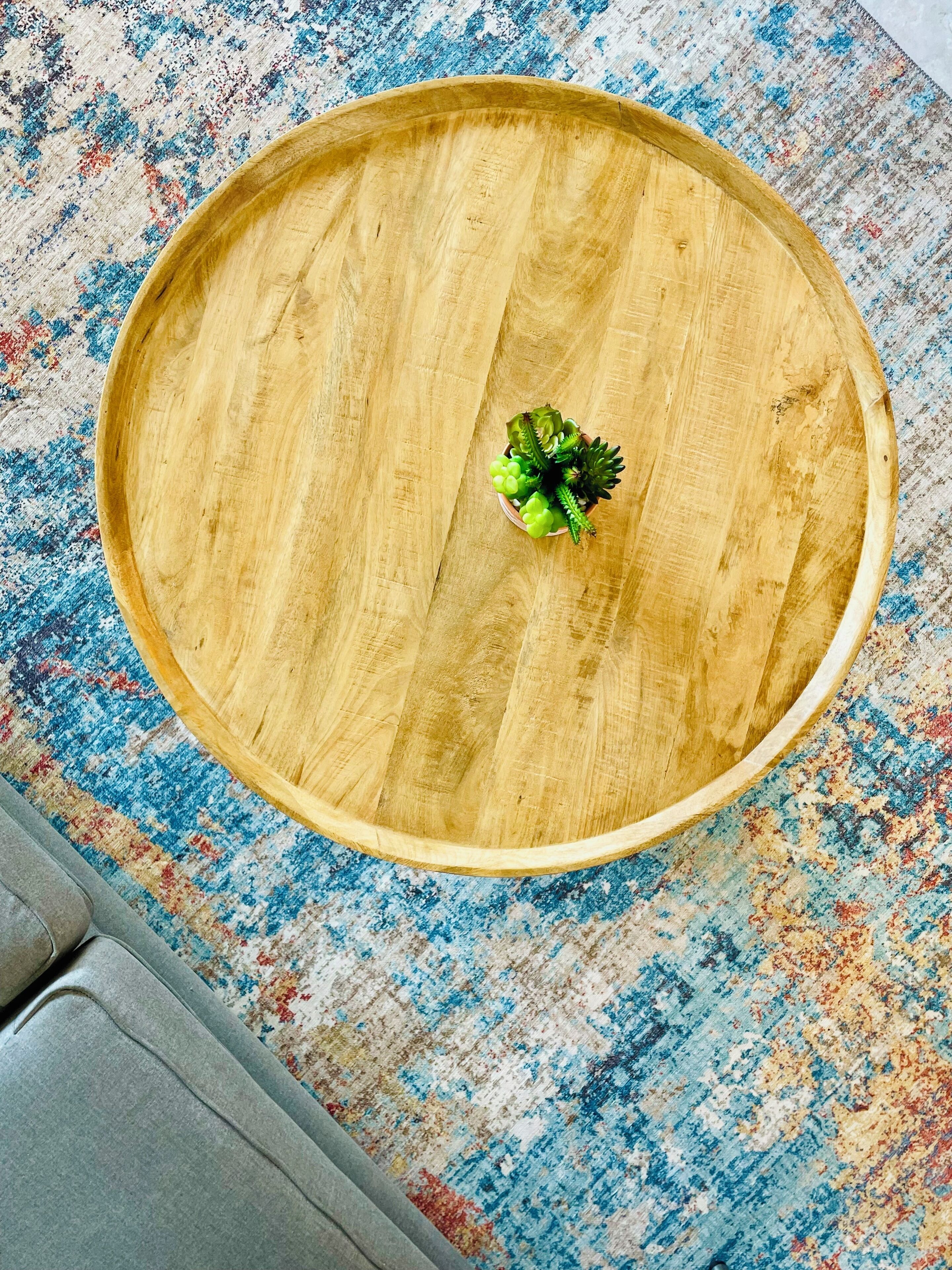 A round wooden table with a small potted plant on a patterned rug.