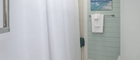 A bathroom with a shower curtain, a towel rack with two towels, and a painting of the ocean on the wall.