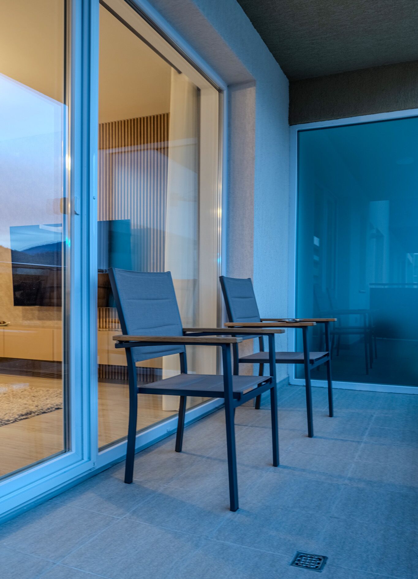 A modern room with two chairs near a sliding glass door, a flat-screen TV, and a wooden table.