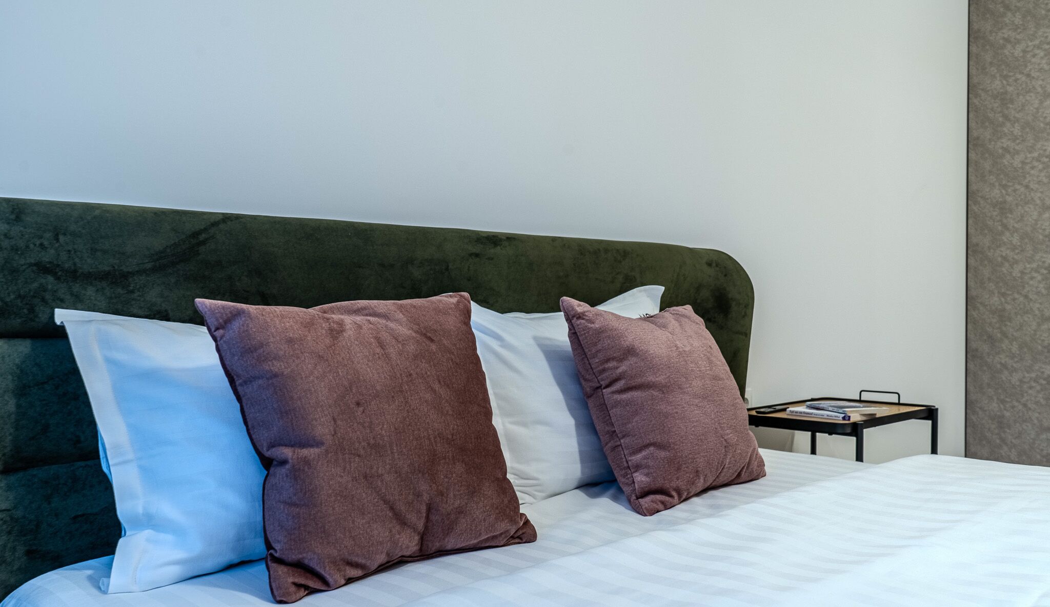A bed with white and brown pillows, a green headboard, and a small bedside table with a book.