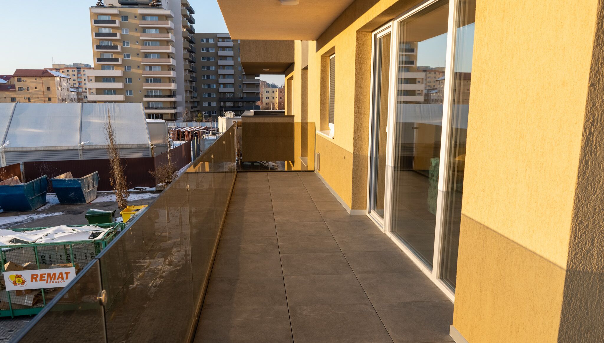 A balcony with a view of a cityscape, a trash bin, and a sign reading "REMAT BRASOV".