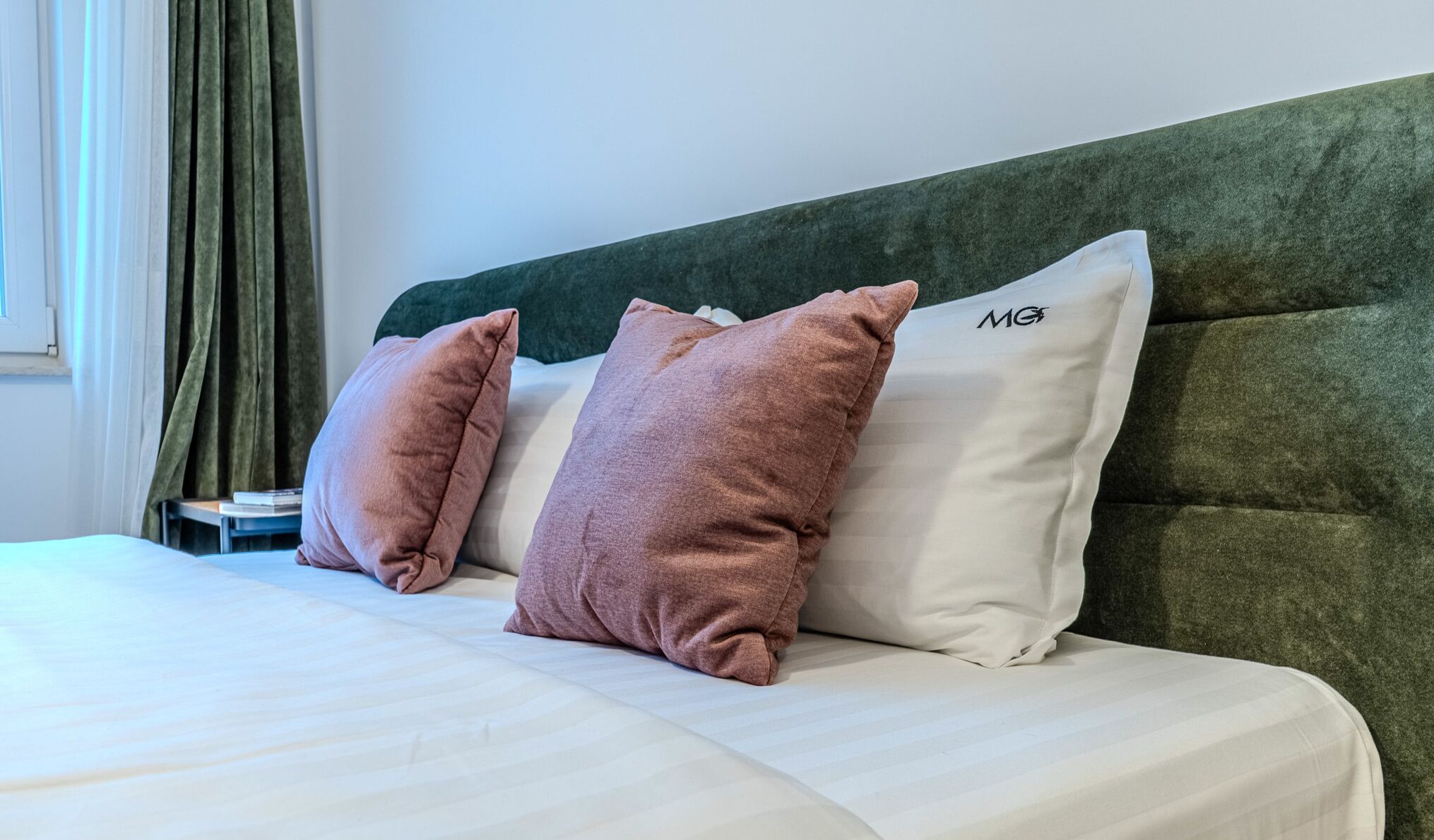 A bed with a green headboard, two pillows, and a white blanket.