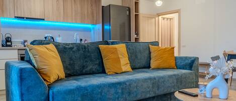 Una sala de estar moderna con un sofá azul, armarios de madera, una zona de cocina y una mesa de comedor.