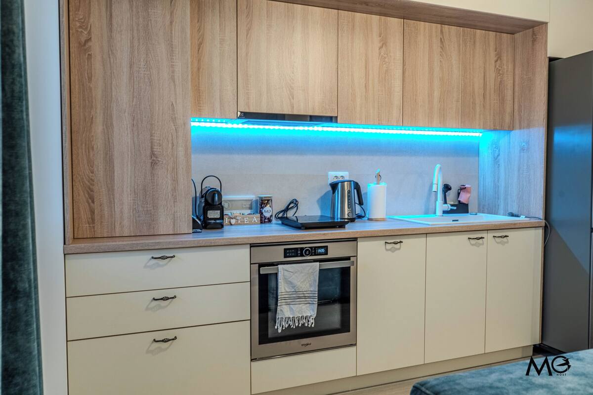 A modern kitchen with wooden cabinets, a built-in oven, and a countertop with a coffee maker and kettle.
