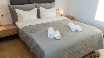 A neatly made bed with a grey quilt, two pillows, and two rolled towels on the bed.