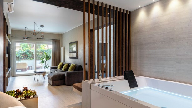 A modern bathroom with a large bathtub, a wooden partition, and a view of a living area with a sofa and a dining table. - Pool & SPA Vatican Luxury Apt (Roma)