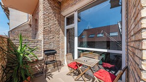 Un patio con pared de ladrillo, una mesa de madera, dos sillas y una parrilla.