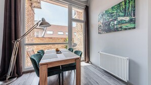 Un comedor con mesa y sillas, un radiador, una ventana con cortinas y un cuadro en la pared.