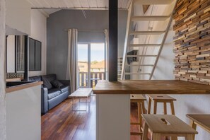 A modern interior with a sofa, wooden tables, a staircase, and a view through a glass door.