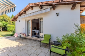 Eine Terrasse mit Tisch und Stühlen, eine Glastür und ein kleiner Gartenbereich.