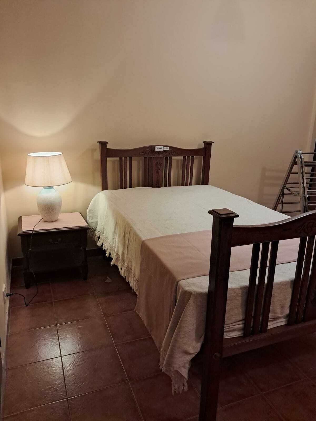 Un dormitorio con una cama, una mesita de noche con lámpara, un cabecero de madera y una escalera apoyada en la pared.